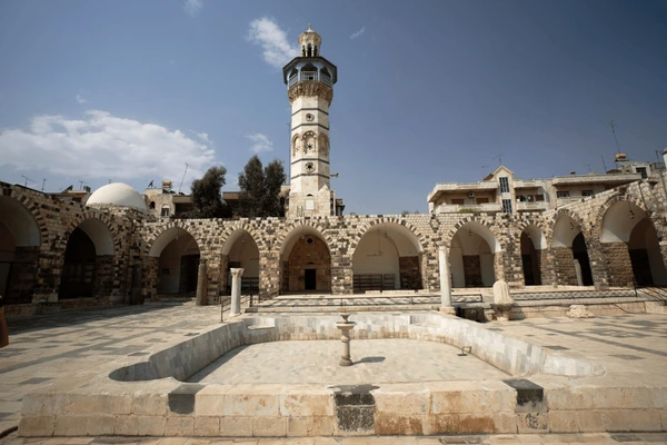 صحن الجامع الأعلى الكبير في مدينة حماة، تظهر فيه الأروقة ذات الأقواس الحجرية والمئذنة الحجرية وبركة الوضوء في وسط الصحن.